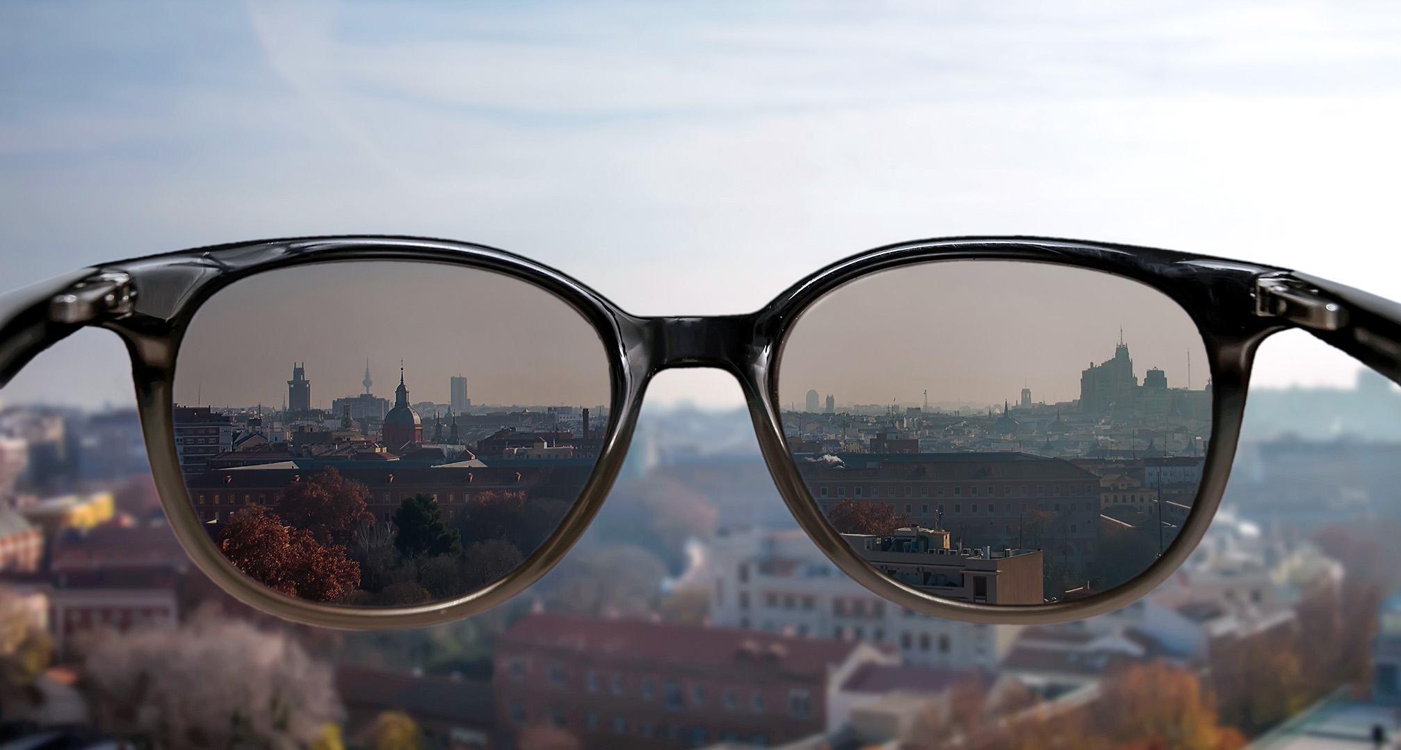 solglasögon hålls framför stadsbild i bakgrunden